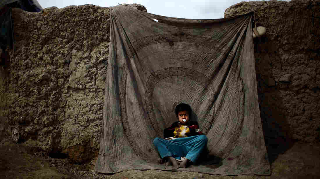 A boy sits blowing bubbles against a blanket used as a door to a home in the Nasaji Bagrami camp for internally displaced Afghans in Kabul.