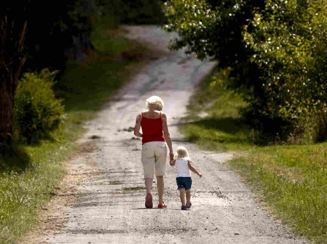 An adult and a child walk down a gravel road.