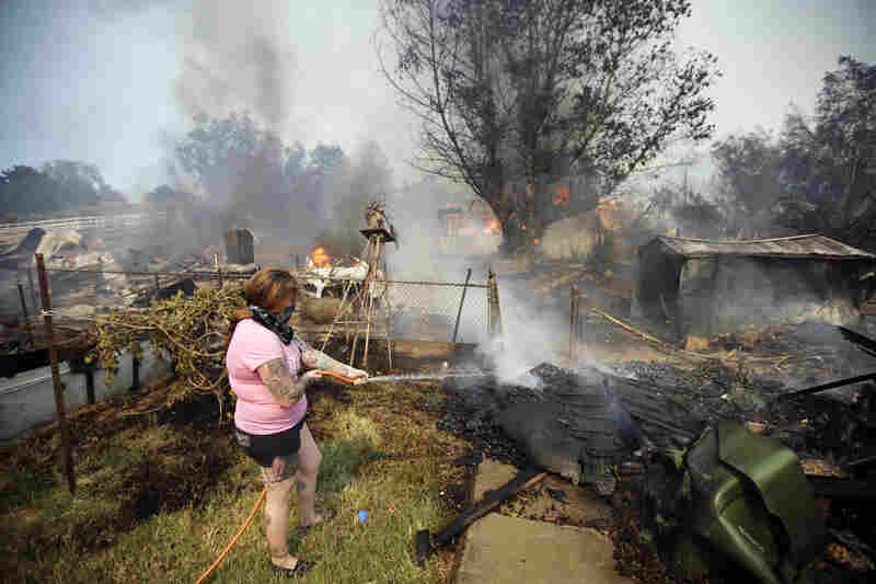 A woman douses debris around her home as her neighbor's home burns Thursday in Escondido. 