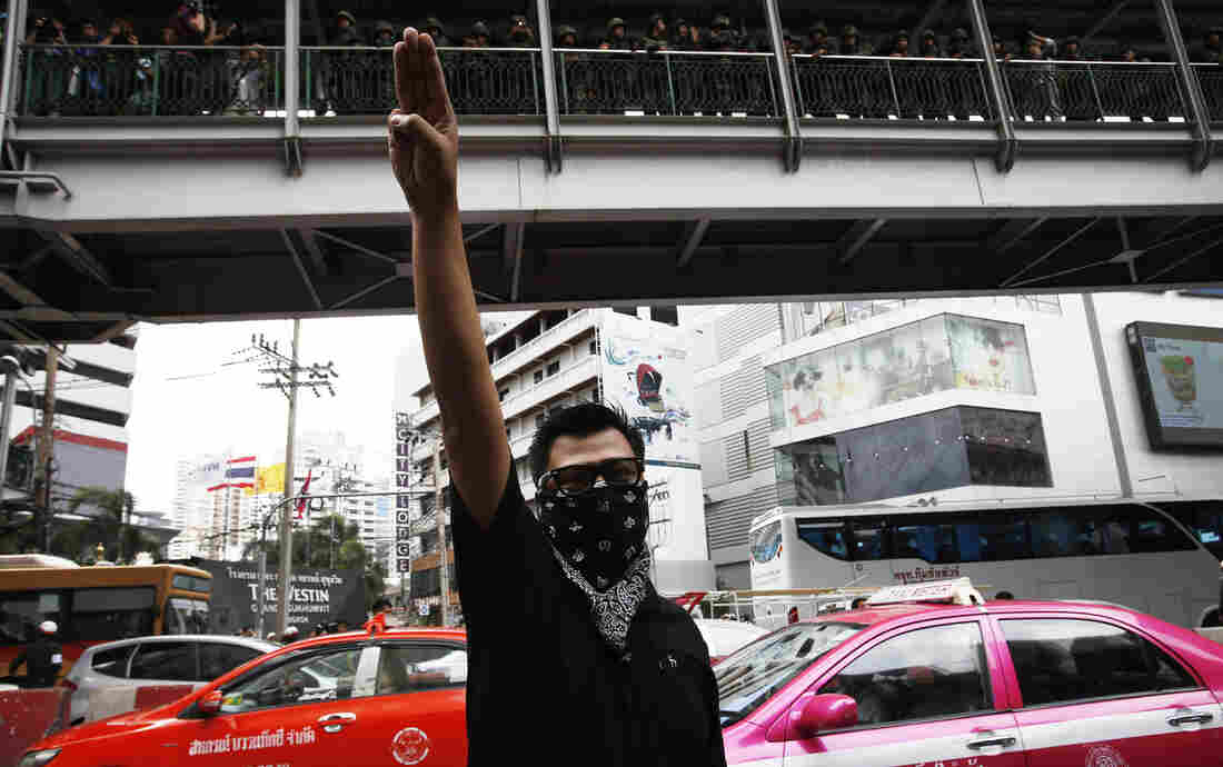 A protester against military rule holds up his three middle fingers as soldiers look on from above during a brief demonstration outside a shopping mall in Bangkok on Sunday. Demonstrators adopted the gesture from The Hunger Games.
