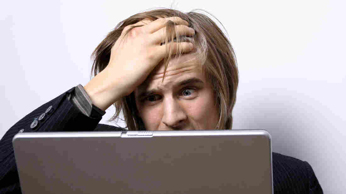A man puts his hand to his forehead as he looks at a laptop computer screen.
