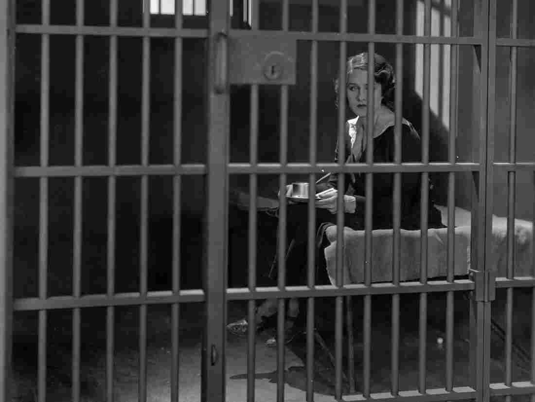 Circa 1925: A prisoner stares forlornly through the bars of her prison cell.