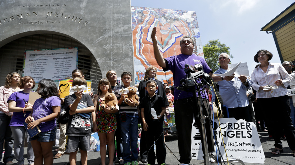 Human-rights activist Enrique Morones, at podium, speaks during a rally in support of immigrants on Wednesday in San Diego. A group of about 70 people rallied in support of migrant children and families Wednesday, a day after U.S. Homeland Security buses carrying the migrants were routed away from American flag-waving protesters in Murrieta, Calif., and transported to a facility in San Diego. (Gregory Bull/AP)