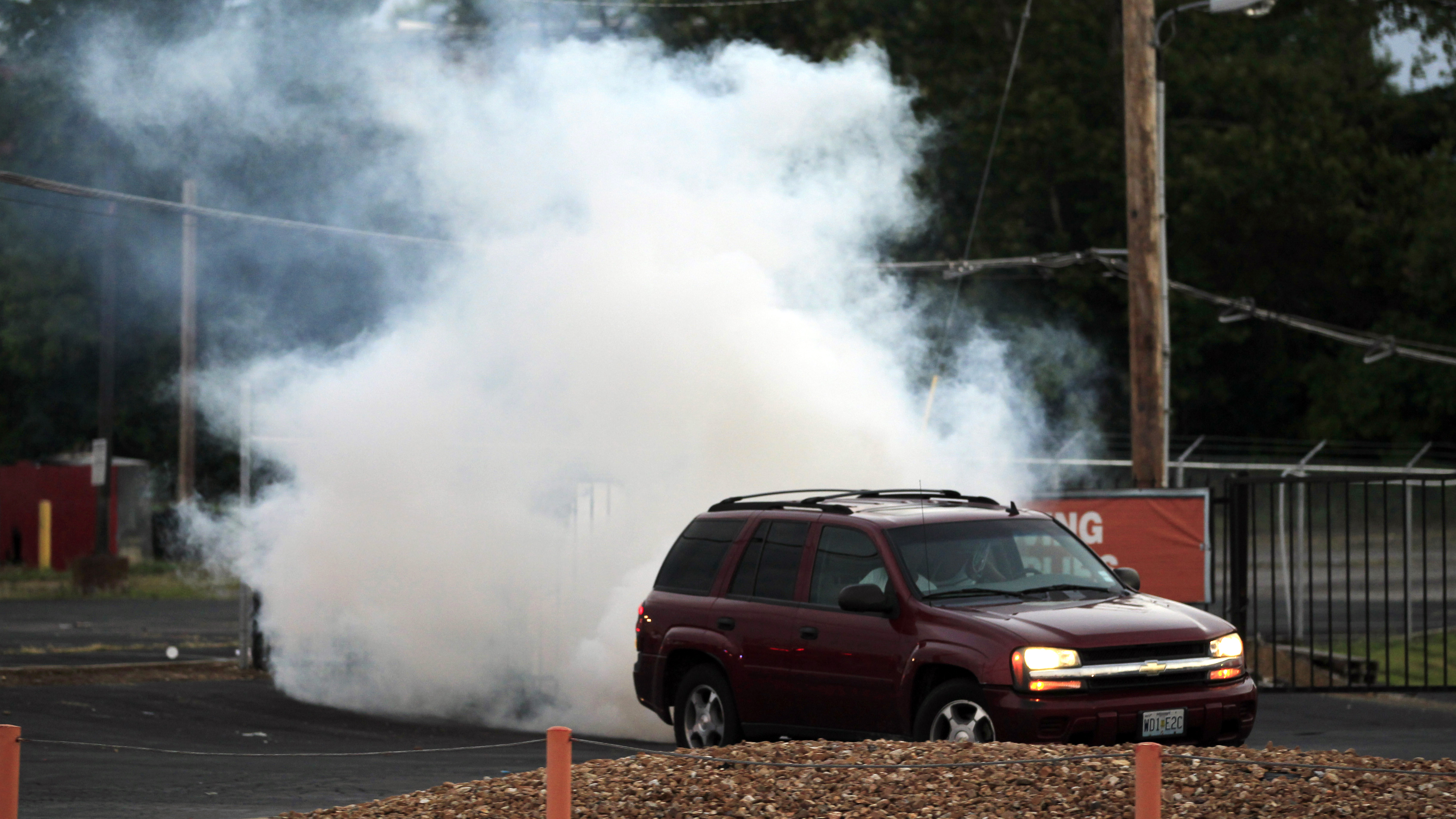 A car pulls away as tear gas is deployed by police in Ferguson, Mo., Monday, in an effort to quell unrest and looting in the wake of the death of teenager Michael Brown.