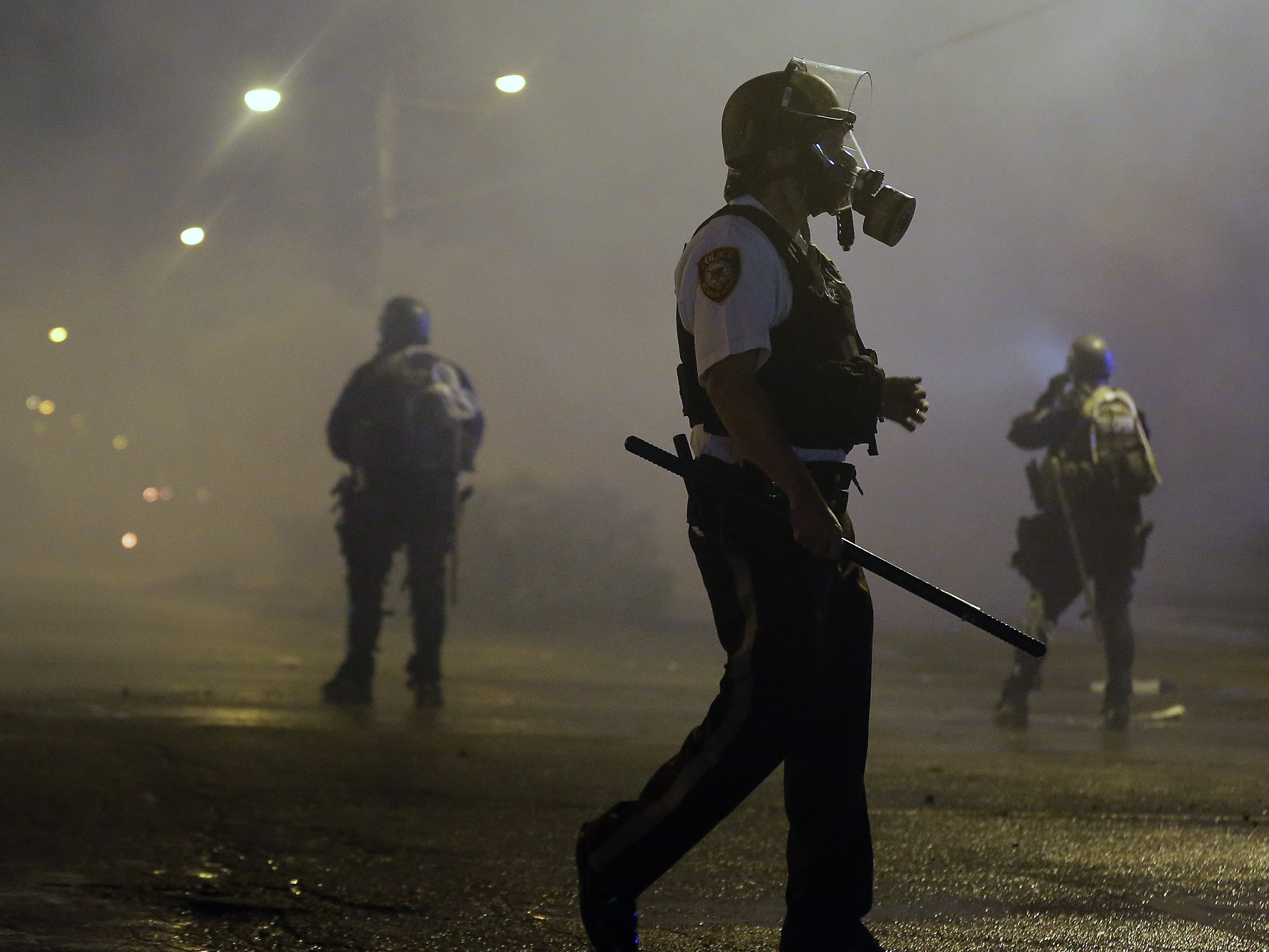 Law enforcement officers wait to advance Sunday morning after firing tear gas to disperse a crowd protesting the shooting of teenager Michael Brown in Ferguson, Mo. Authorities report one shooting and several arrests.