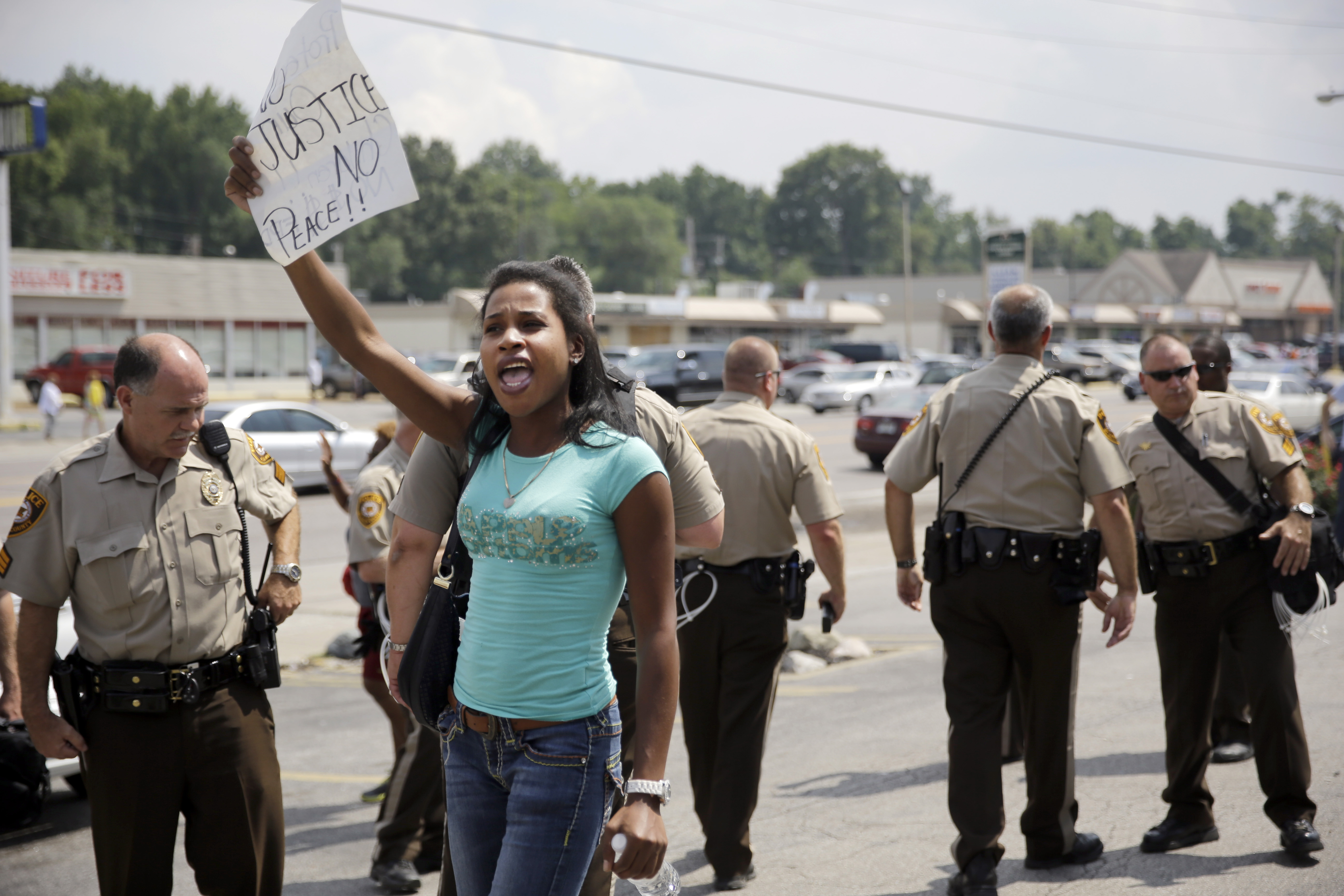 A protester holds up a sign as police try to keep protesters and media moving.