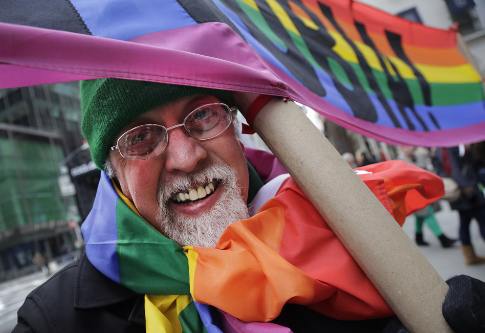Artist Gilbert Baker, designer of the Rainbow Flag, is draped with the flag while holding a banner that reads "Boycott Homophobia" before the start of the St. Patrick's Day parade in March in New York. (Mark Lennihan/AP)