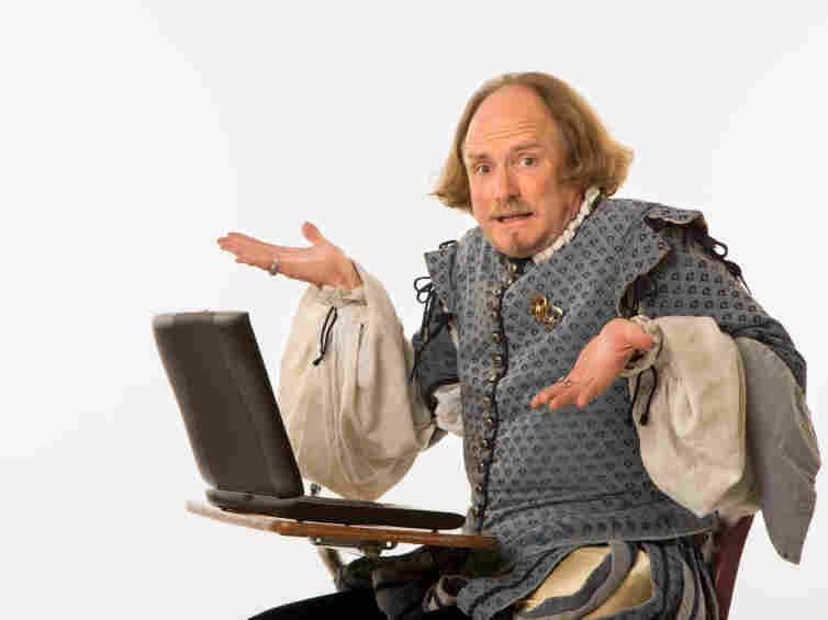 William Shakespeare in period clothing sitting in school desk with laptop computer shrugging at viewer.