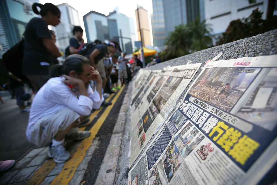 People read newspapers placed along a street blocked by protesters outside the government headquarters building in Hong Kong on Wednesday. While Hong Kong media are covering the protests closely, media in mainland China have been mostly quiet. (Carlos Barria/Reuters/Landov)