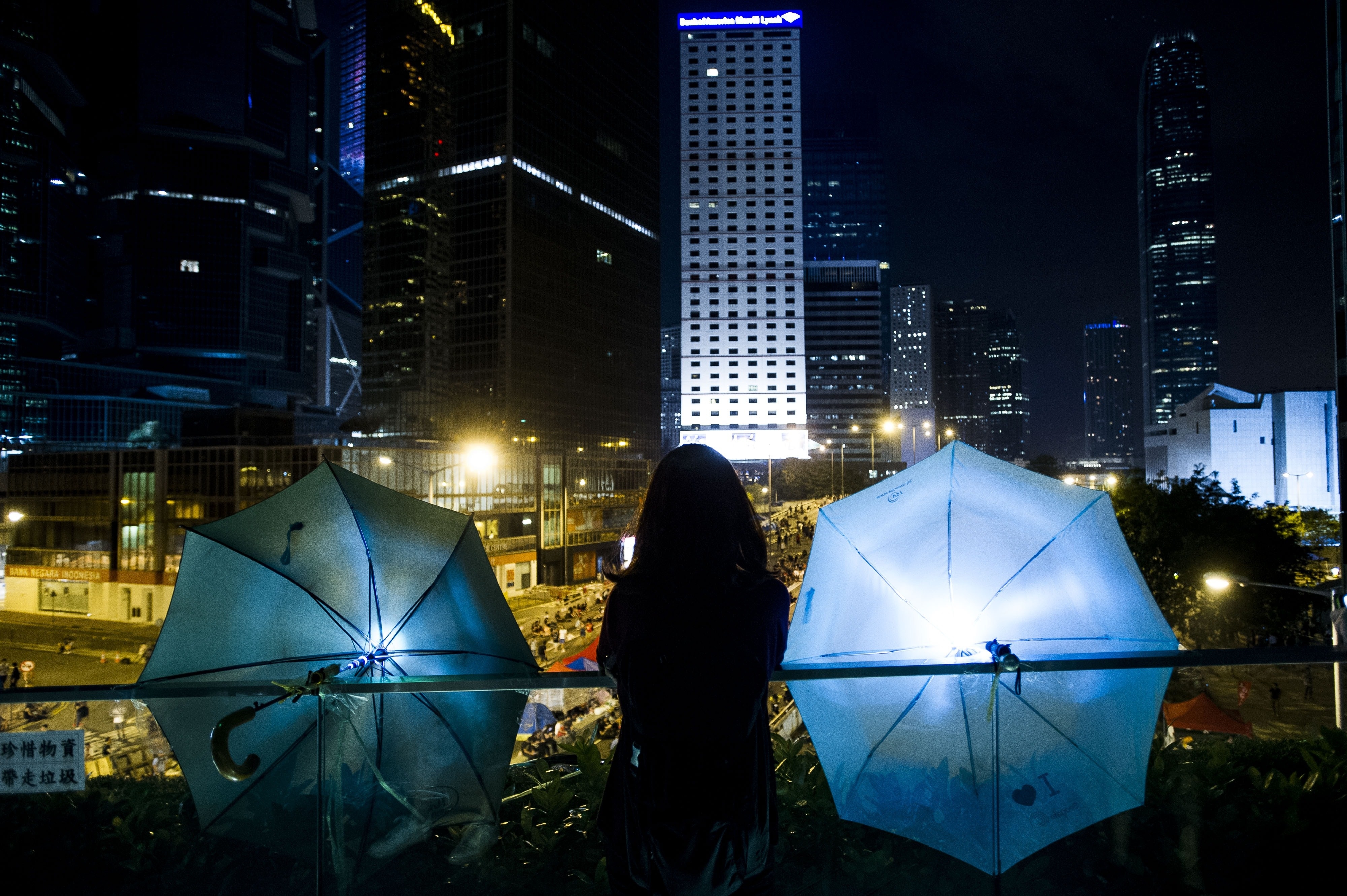 A woman stands between two umbrellas as she looks over the bridge to Admiralty district on Sunday in Hong Kong.