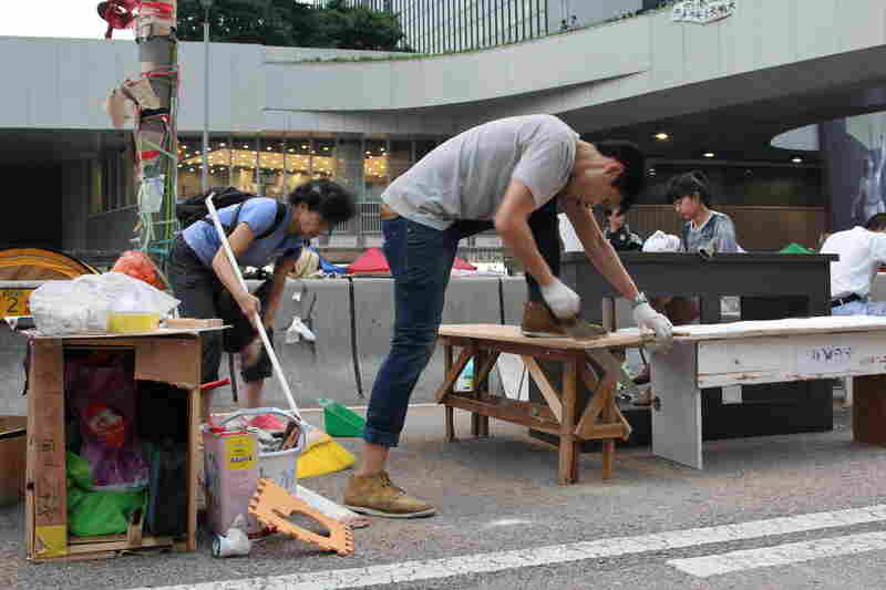 People with no past carpentry experience jump in to build tables and chairs from scrap wood so the students can continue their studies while protesting.