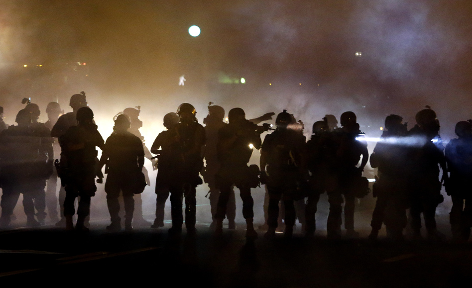 Police walk through a cloud of smoke as they clash with protesters in Ferguson, Mo., this summer. (Jeff Roberson/AP)