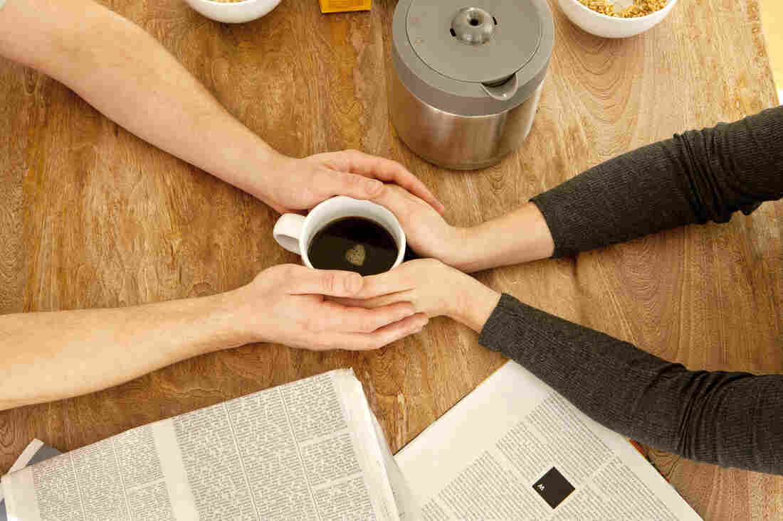 Couple's hands wrapped around one cup of coffee.