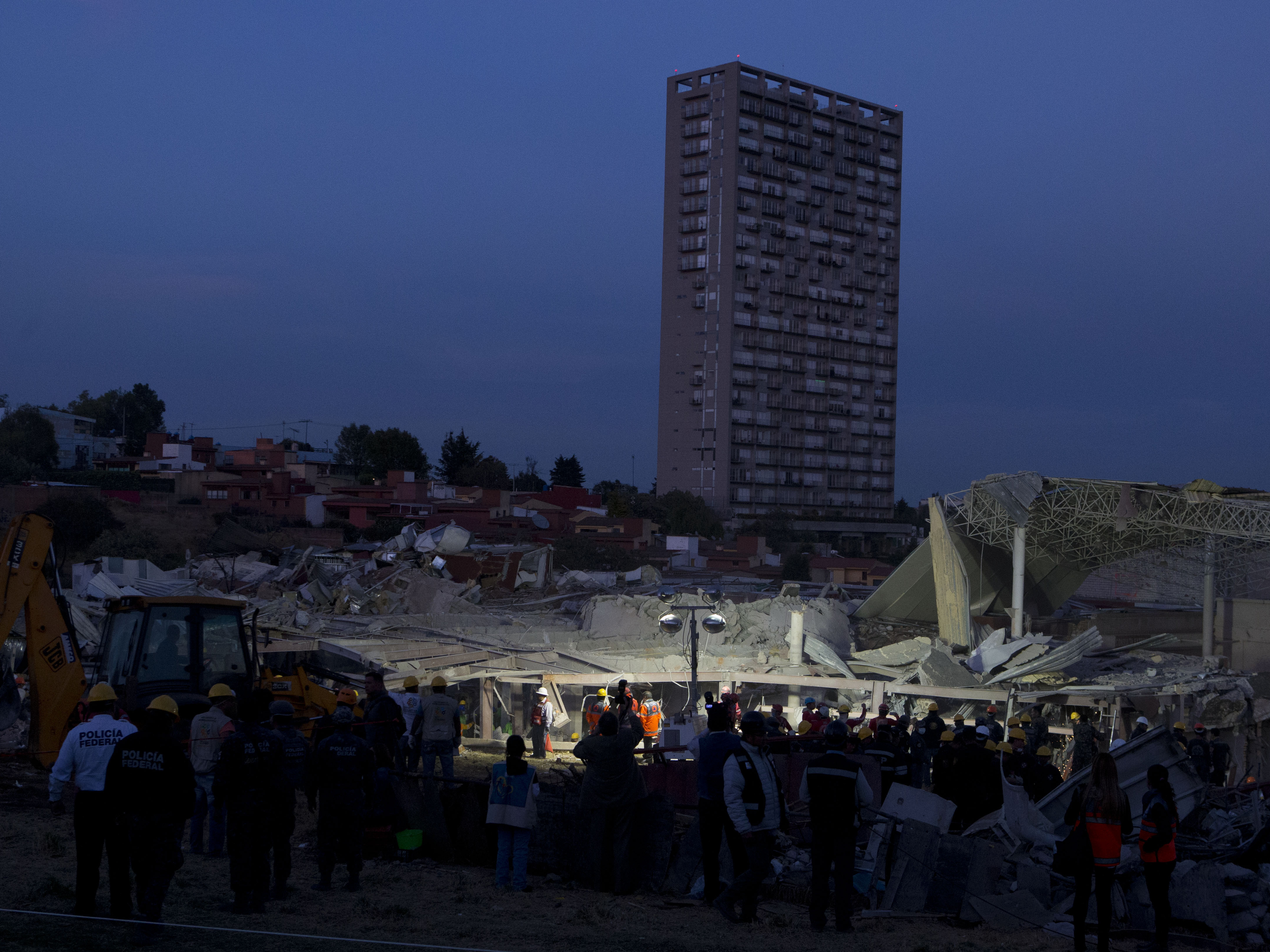 Rescue workers and police stand around the scene Thursday night as the search for survivors continues among the wreckage of a maternity and children's hospital in Cuajimalpa on the outskirts of Mexico City.