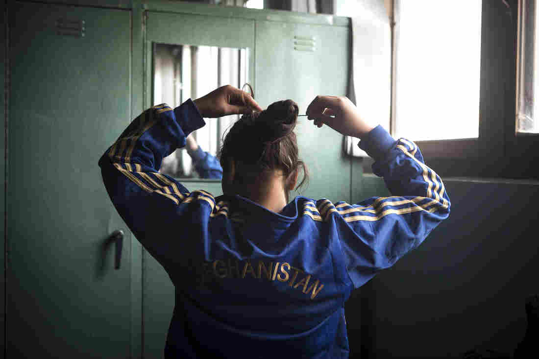 At the Spartan gym with no bathroom or showers, a girl puts up her hair before practice.