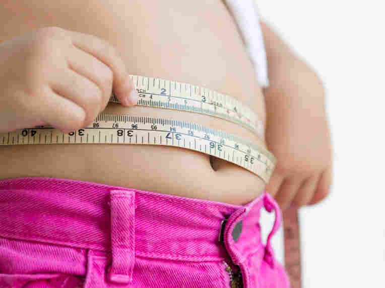 A young girl measures her waist.