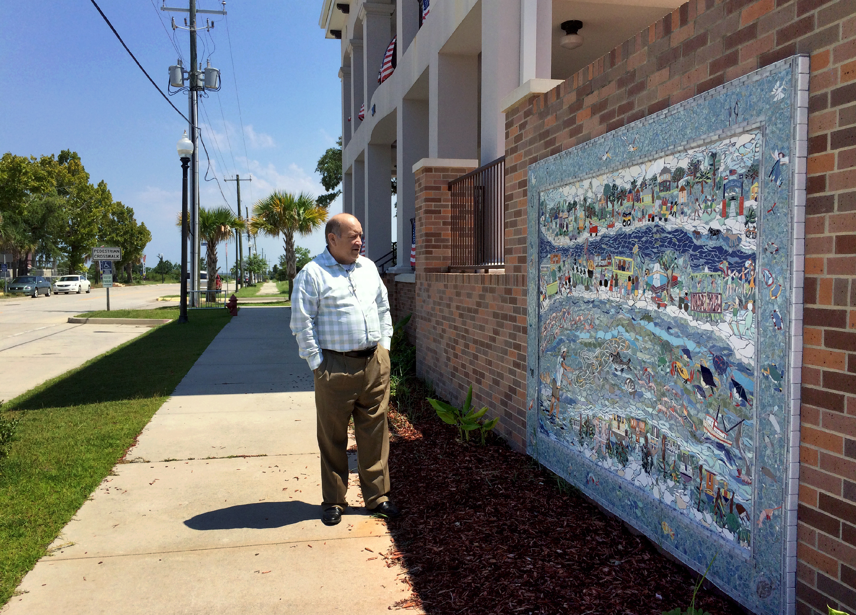 Mayor Mike Smith stands near a mural, created by residents, that depicts Waveland before and after Katrina.