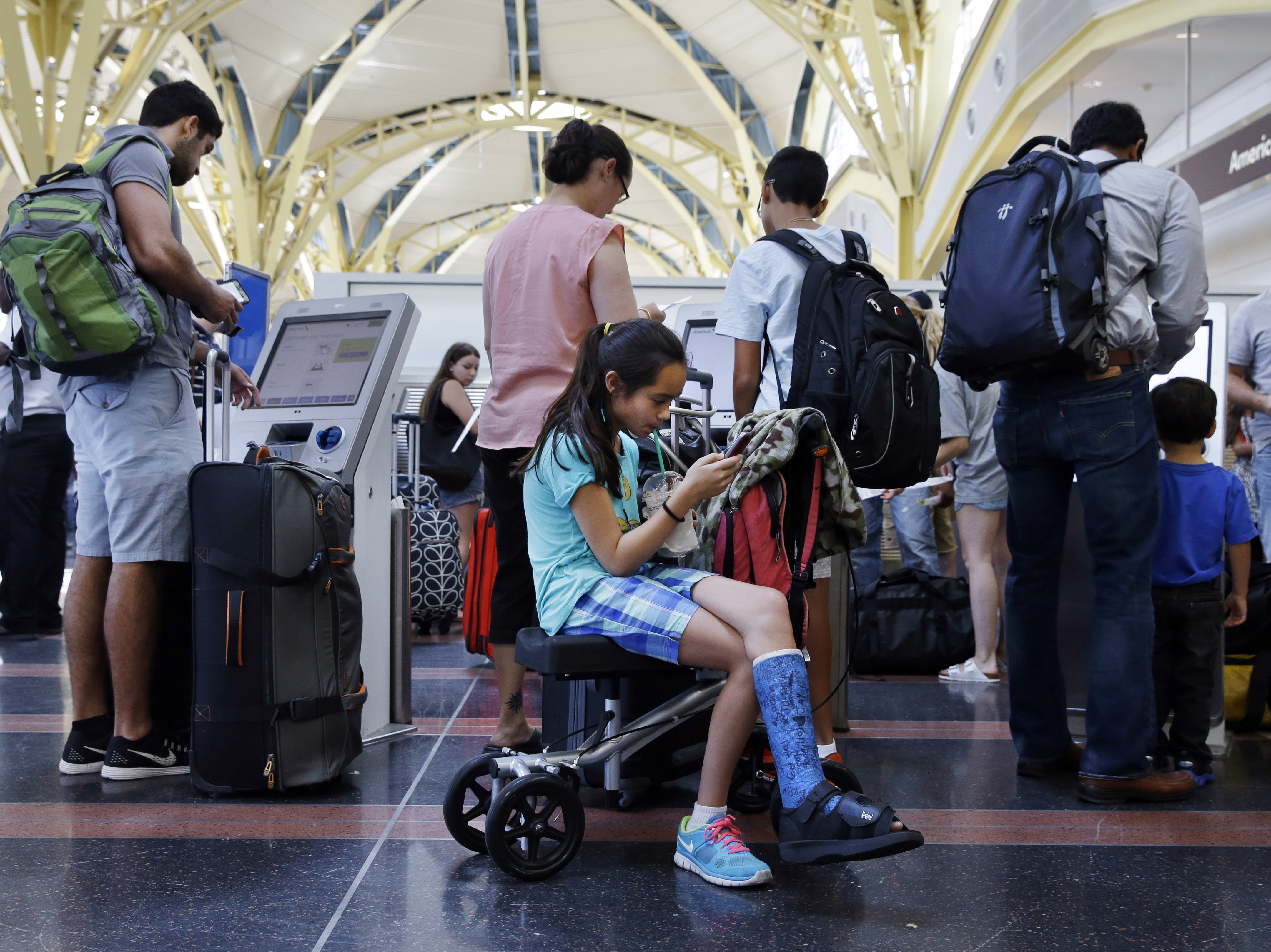 Alisha Lalani, 10, of Ft. Lauderdale, Fla., looks at her phone as her mother and brother check in for their flight to Miami at Washington's Reagan National Airport. Their flight was one of thousands delayed as a result of a technical glitch with an FAA automated system.