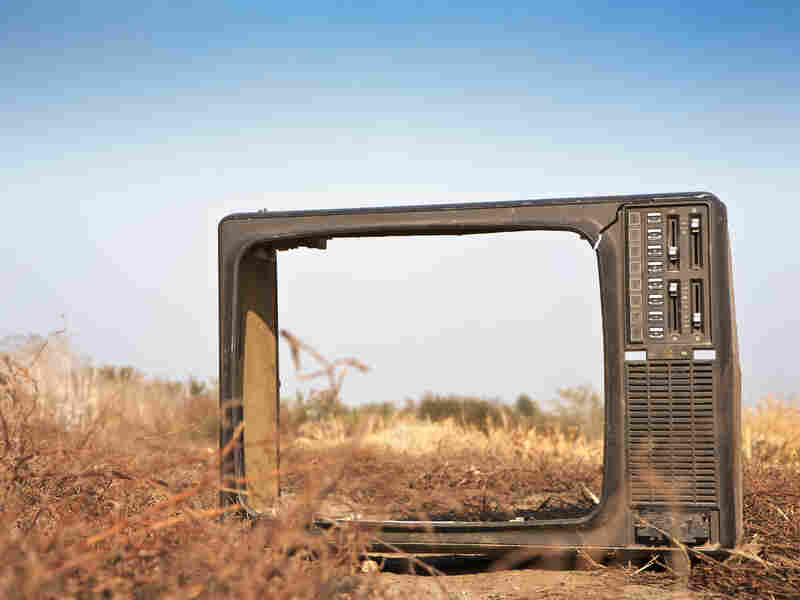 A broken television in a dried-out field.