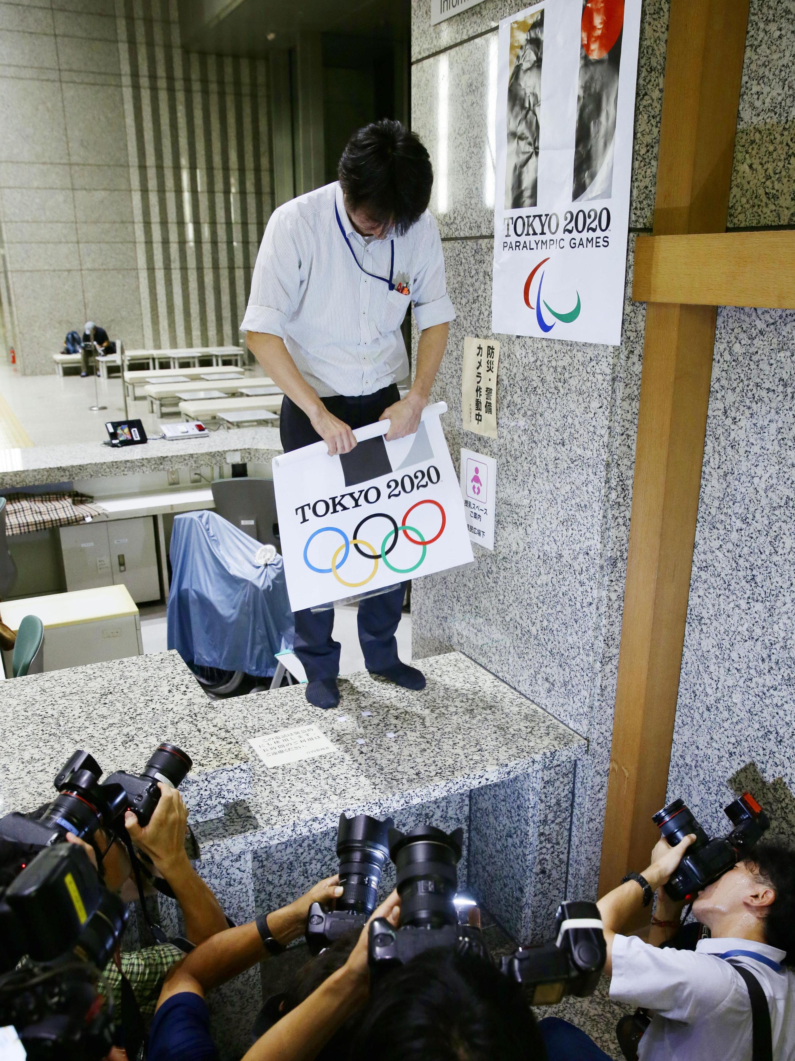 An official of Tokyo's metropolitan government removes a poster bearing logos for the Tokyo Olympic and Paralympic Games from a wall Tuesday. (Kyodo /Landov)