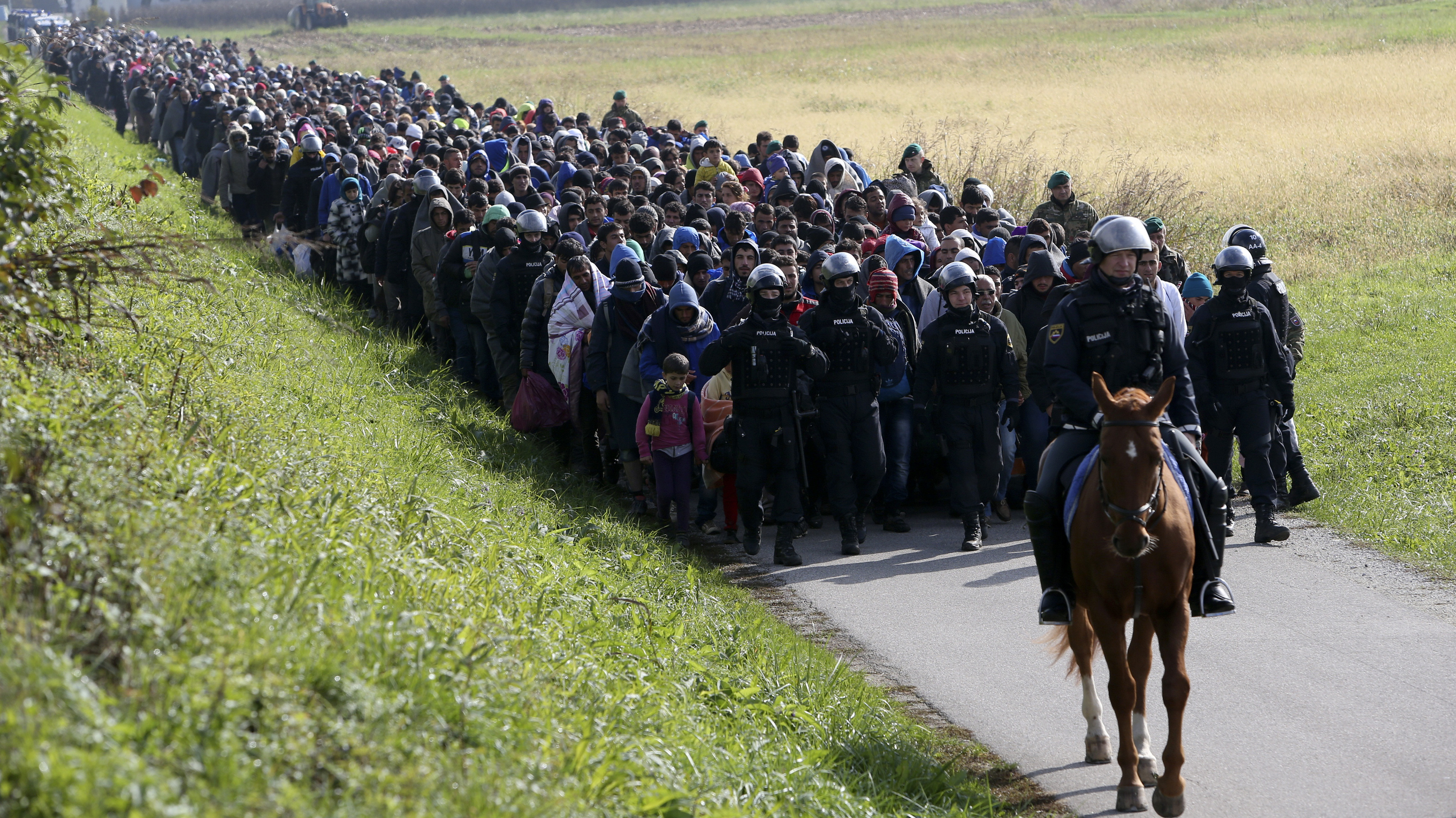 A policeman on horseback and other officers lead a group of refugees and migrants near Dobova, Slovenia, Tuesday. Slovenia's parliament is expected to approve a measure to have the army help police guard the border with Croatia.
