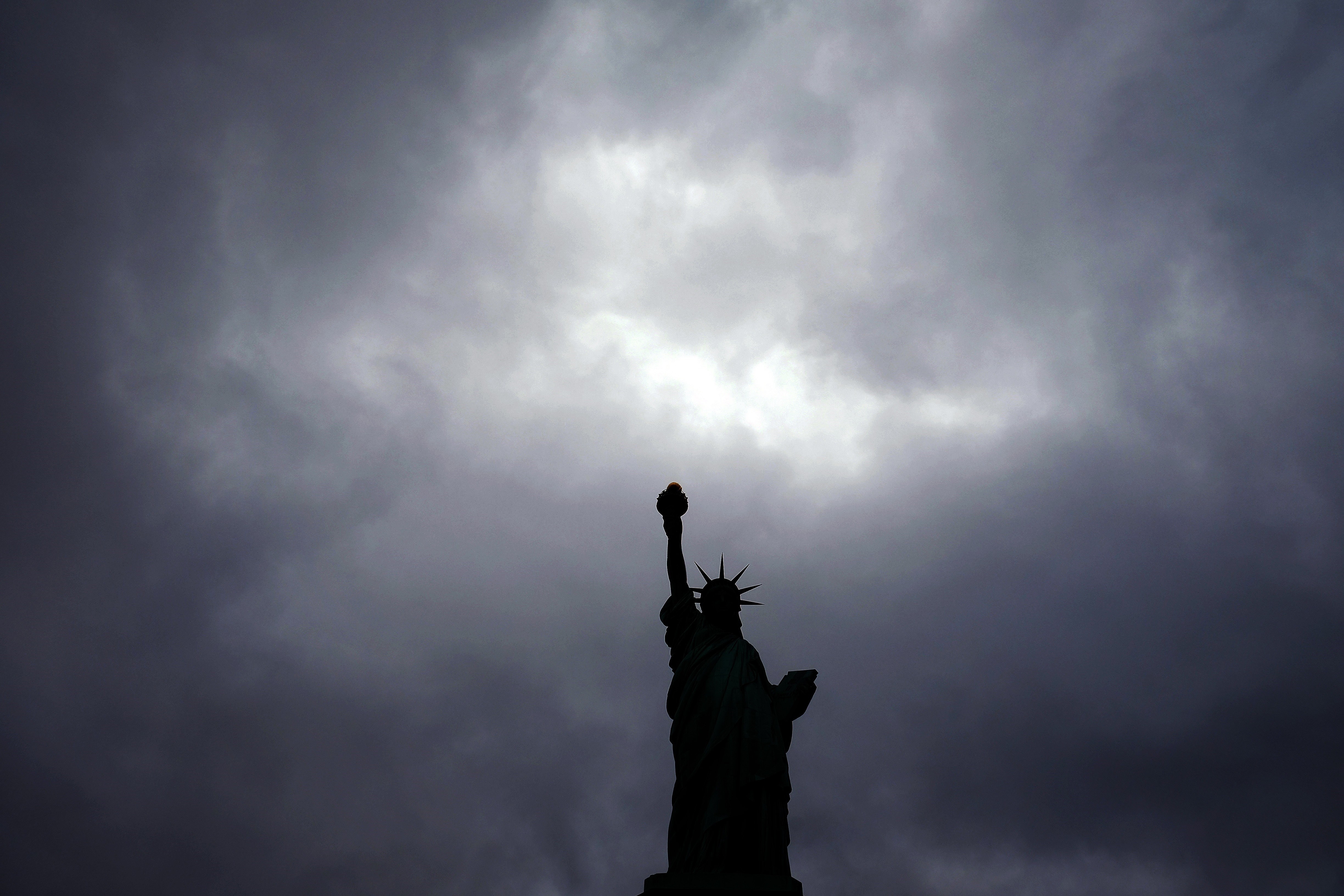 The Statue of Liberty stands tall as dark clouds cover the New York sky.