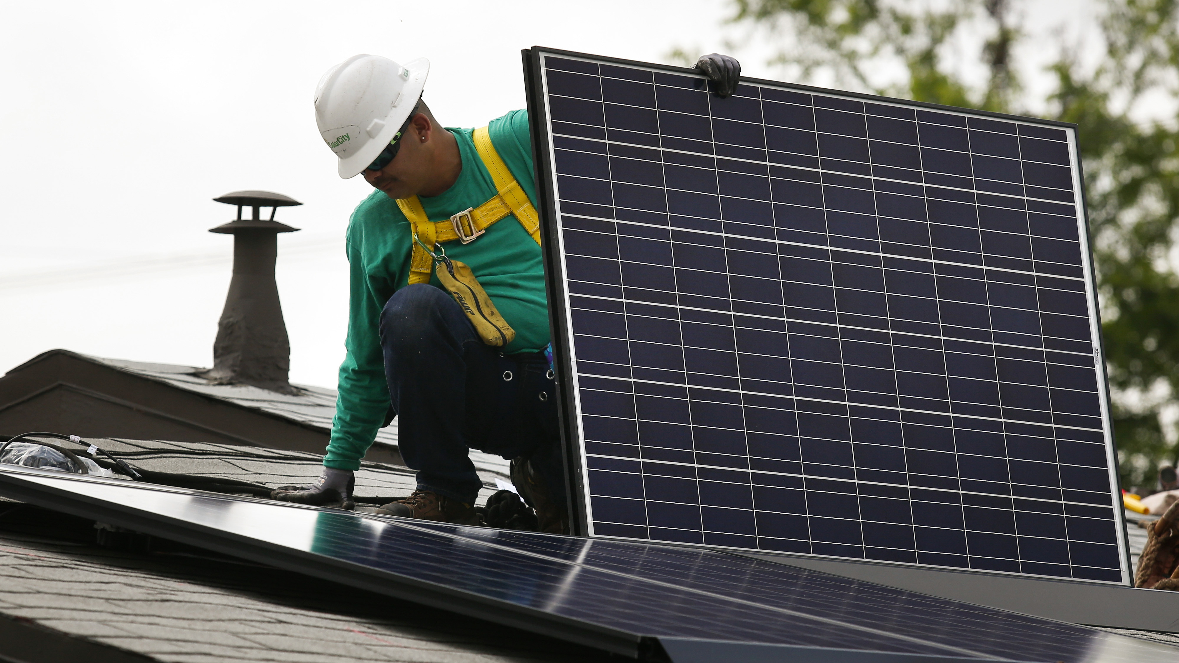 A SolarCity employee installs a solar panel on the roof of a home in Los Angeles in 2014. California's utilities want to pay new solar customers less for their extra electricity and to add new monthly fees. (Bloomberg via Getty Images)