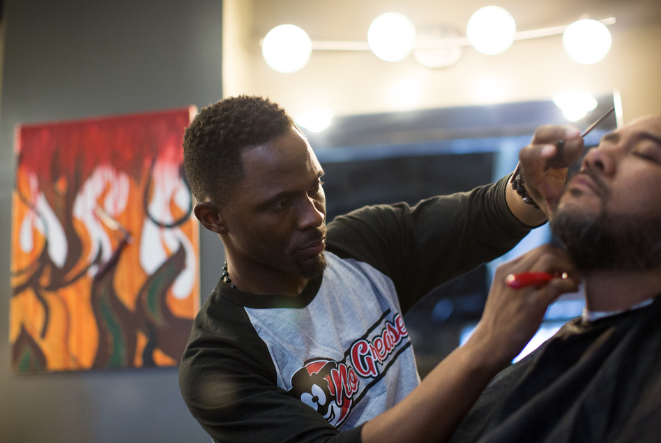 Damian Johnson, owner of No Grease Barber Shop in Charlotte, N.C., finishes up a haircut on Sam Chaney. Sam has been a client for over 10 years. (Logan Cyrus for NPR)