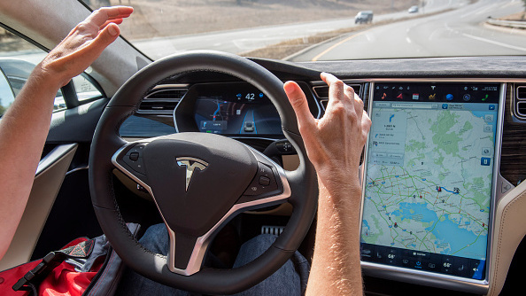 A member of the media tests a Tesla Motors Model S car with an Autopilot system. Regulators and manufacturers are debating whether self-driving cars should have a licensed driver inside as a safety precaution. (Bloomberg via Getty Images)