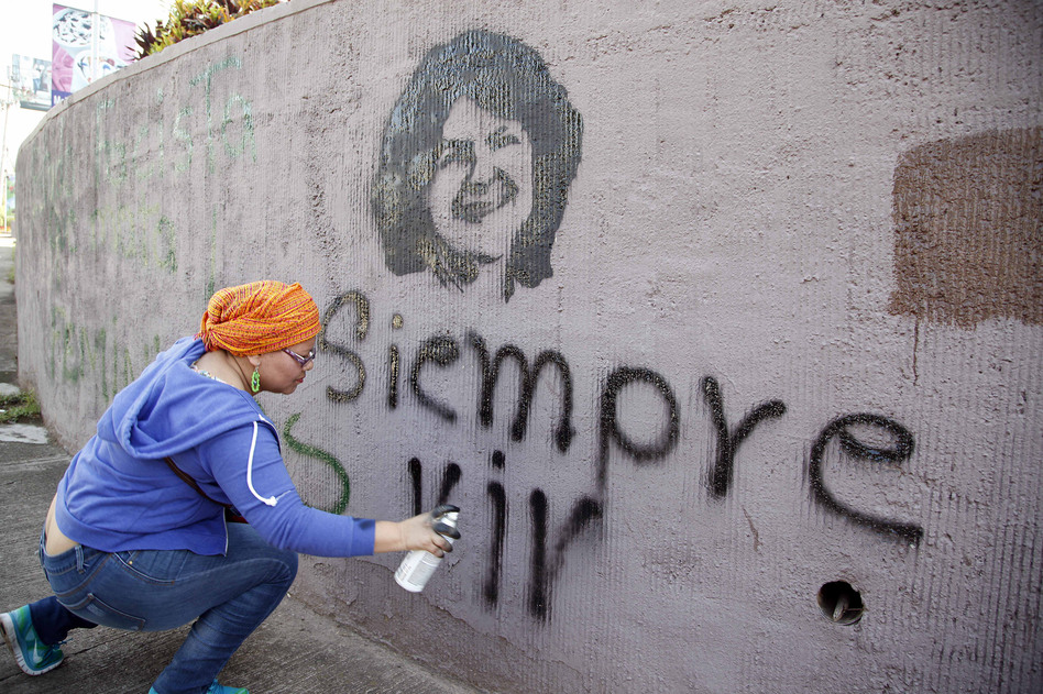 A woman spray paints the phrase "Always Alive" below a stenciled image of slain environmental and indigenous rights activist Berta Cáceres in Tegucigalpa. (Fernando Antonio/AP)