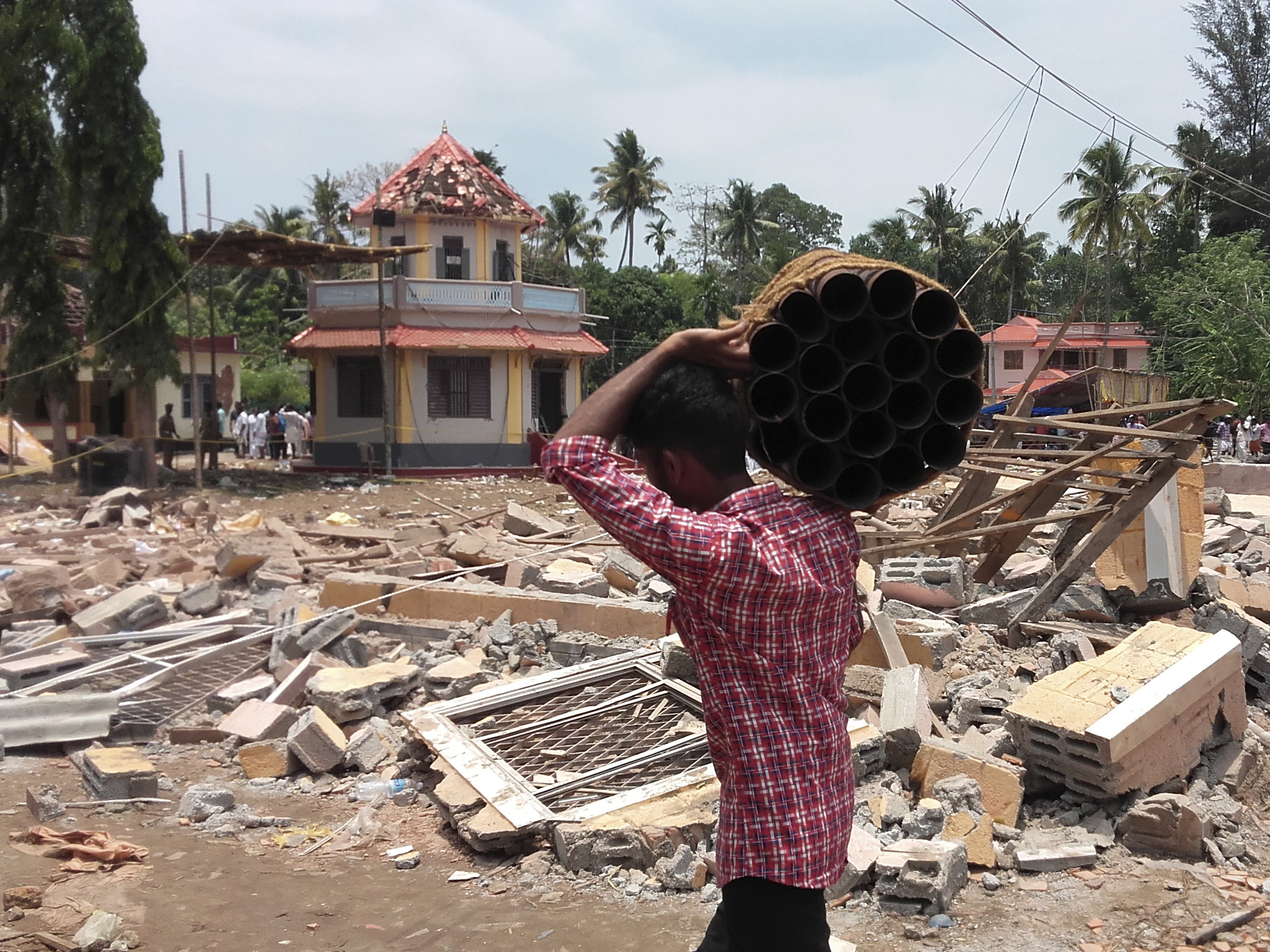 A man carries empty fireworks shells past a collapsed building after a massive fire broke out during a fireworks display at a temple complex in Paravoor village in the state of Kerala, India.