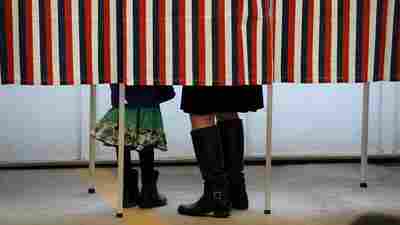 A woman is accompanied by a child inside a voting booth, as she casts her ballot in the New Hampshire presidential primary.