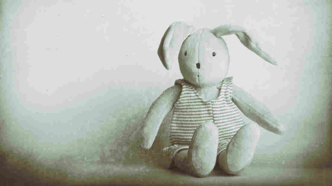 A cute, stuffed children's bunny rabbit toy wearing a striped onesie sitting down against a plain background. Vintage photo style (wet place, monochrome) image with great copy space.