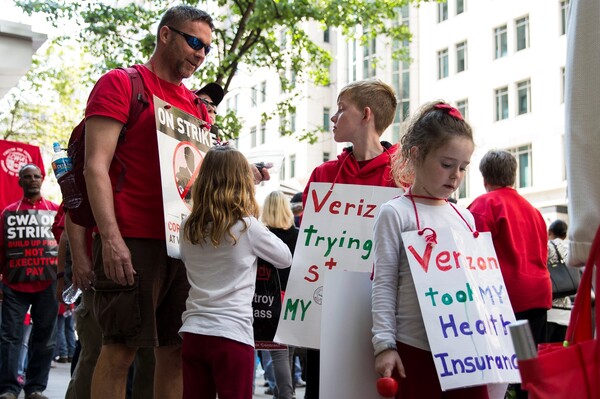 A Verizon worker on strike marches with his children and fellow employees on May 19. With no new contract, workers' health insurance expired at the end of April.