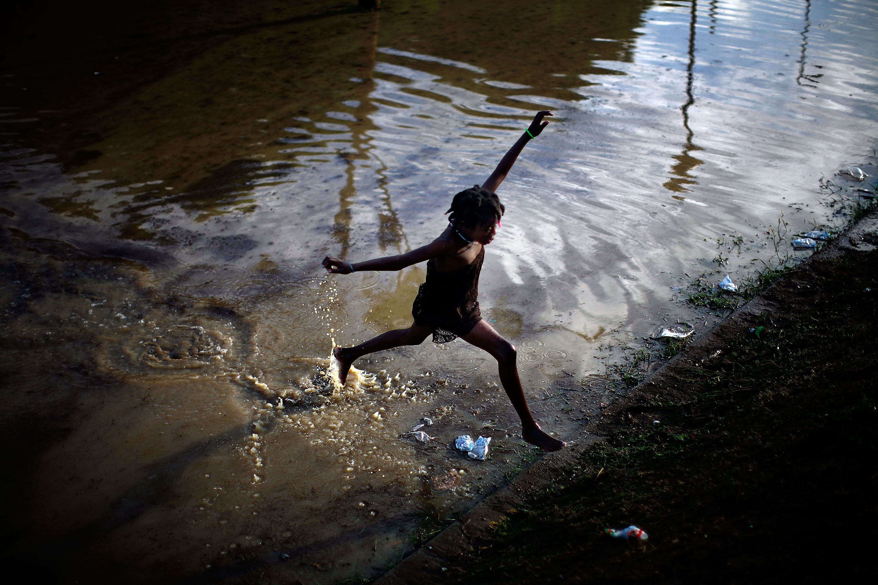 A little girl jumps across a flooded field containing the sewage runoff from the Mais Gate Camp after heavy rains in Port-au-Prince in 2010.