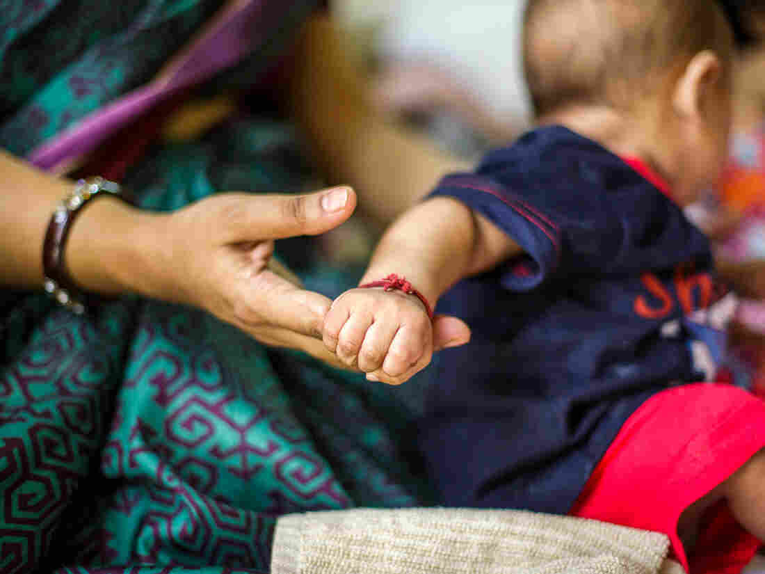 This picture depicts the strong bond between the mother and child. A five (5) to six (6) months old baby holds strongly on his mother's finger, even while his attention is elsewhere.