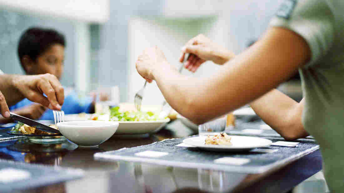 Family sitting around table eating dinner, a woman's arms in the foreground.