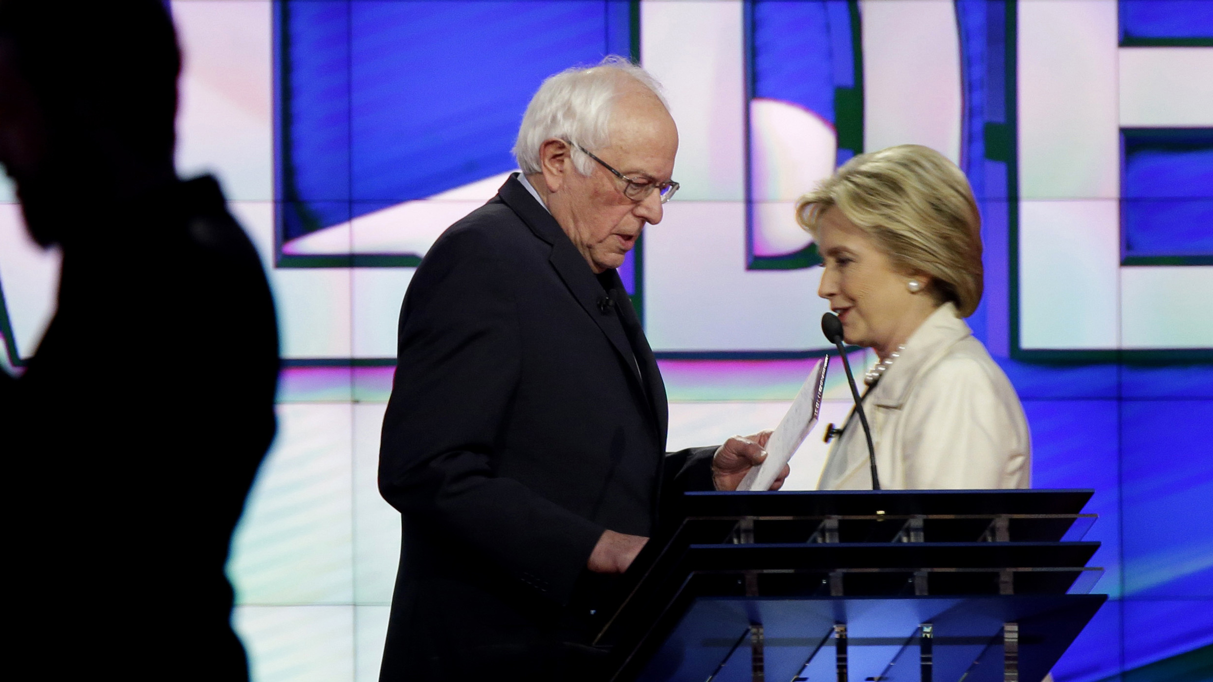 Bernie Sanders and Hillary Clinton pass during a break at a Democratic debate April 14 in New York.