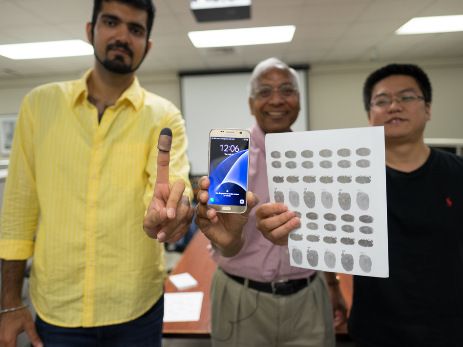 Michigan State University researchers Sunpreet Arora (left), Anil Jain (center) and Kai Cao (right) tried 3-D printed fingertips and 2-D fingerprint replicas on conductive paper to unlock a murder victim's phone, similar to one in the photo. (Derrick Turner/Michigan State University)
