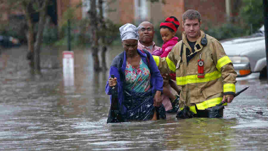 A member of the St. George Fire Department assists residents as they wade through floodwaters from heavy rains in Baton Rouge, La. on Friday.