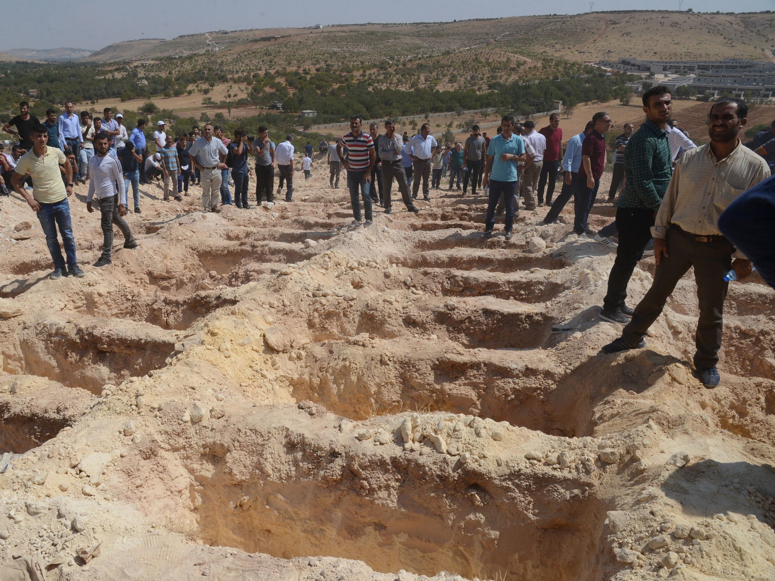 People wait close to empty graves at a cemetery on Sunday, during the funeral for the victims of a suicide attack on a wedding party in Gaziantep, Turkey. At least 50 people were killed when a suspected suicide bomber linked to Islamic State jihadists attacked a wedding thronged with guests, officials say.