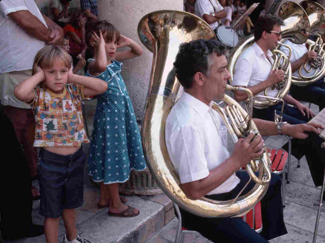 Children cover their ears while listening to a brass band perform.