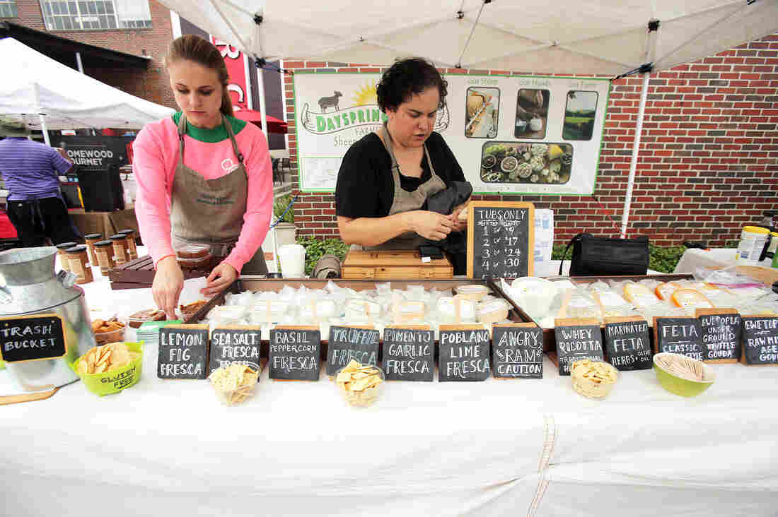 Ana Kelly, with Melody Weldon, a part-time employee, quickly gets the booth ready for business at Pepper Place Market, held on Saturdays in Birmingham, Ala. Names of the cheeses reflect the ingredients.