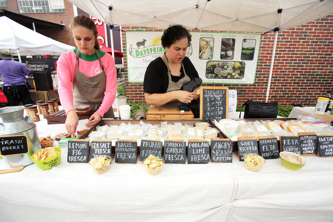 Ana Kelly, with Melody Weldon, a part-time employee, quickly gets the booth ready for business at Pepper Place Market, held on Saturdays in Birmingham, Ala. Names of the cheeses reflect the ingredients.