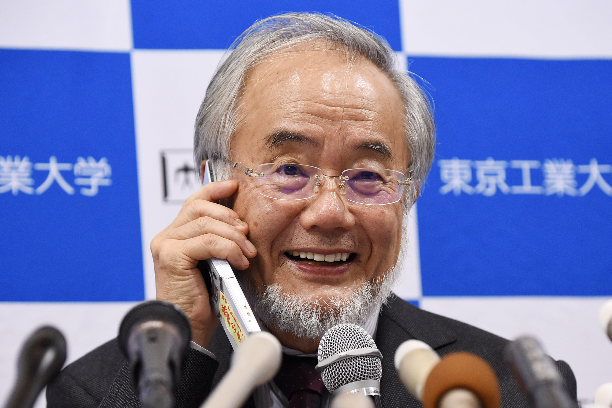 Yoshinori Ohsumi, a professor at the Tokyo Institute of Technology, smiles as he speaks with Japanese Prime Minister Shinzo Abe on a phone during a press conference in Tokyo today, after he was awarded the Nobel Medicine Prize.