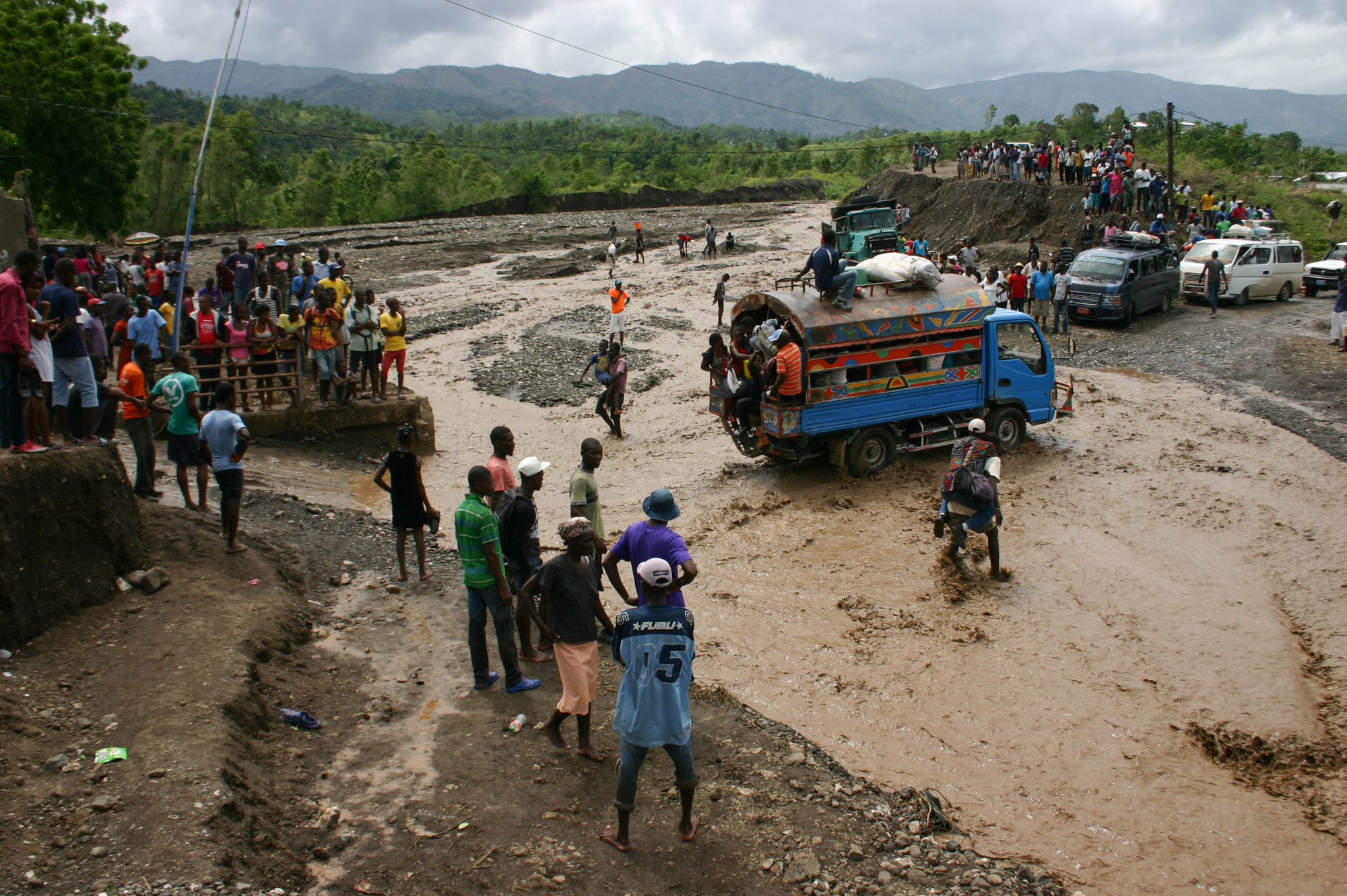 Haitians watch as people cross a river on National Route 2. Hurricane Matthew washed out a bridge at this spot cuttting off much of the southwest of the country from the capital Port au Prince. (NPR)