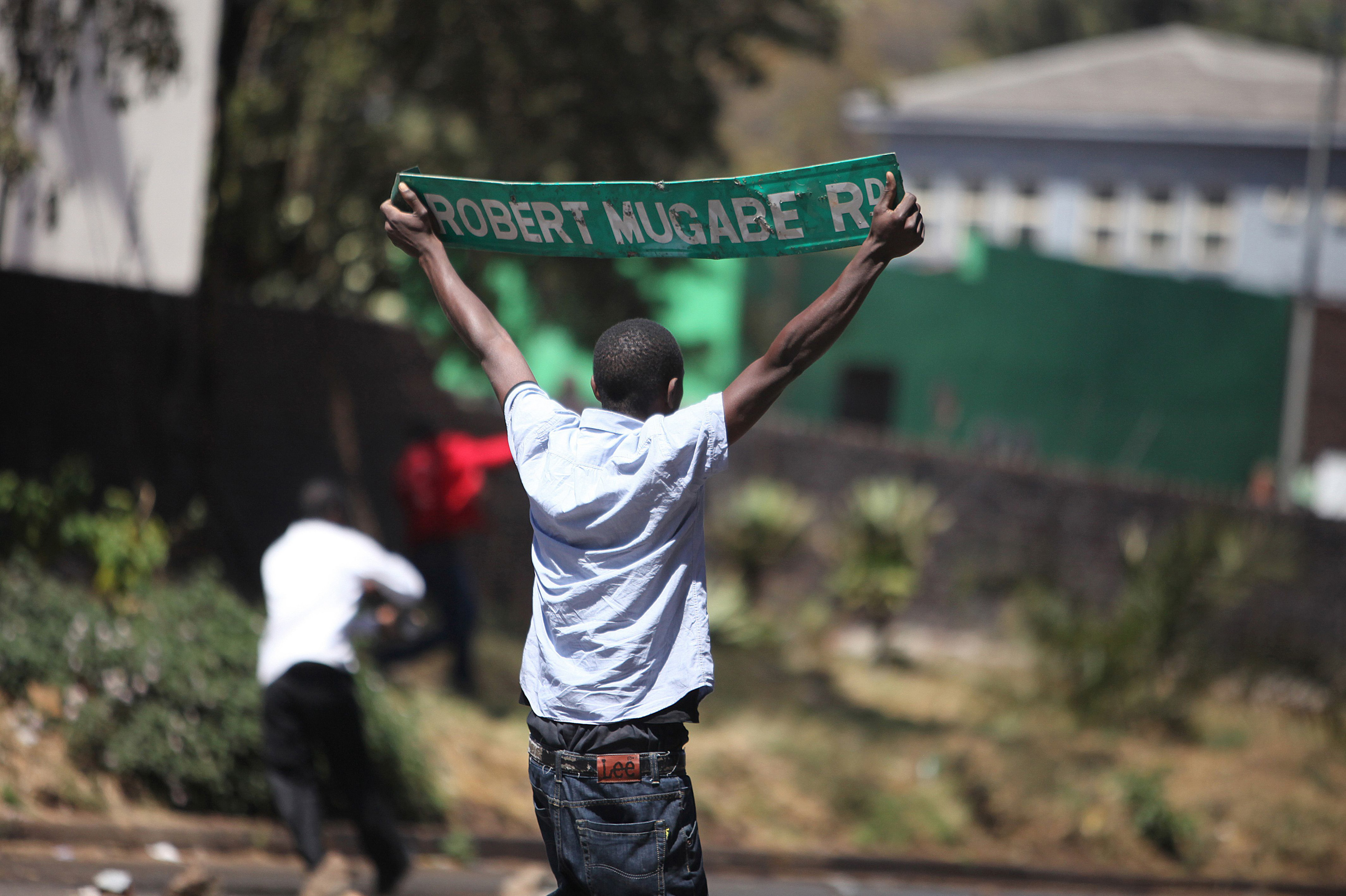 A protester holds up a street sign with President Robert Mugabe name on it as Zimbabwe opposition supporters clash with police during a protest march for electoral reforms on August 26, 2016 in Harare. Riots erupted in Zimbabwe's capital Harare after police fired tear gas and beat protesters who responded by throwing stones in the latest of a string of tense demonstrations. (AFP/Getty Images)