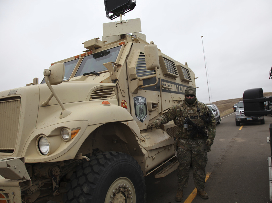 A member of the Stutsman County SWAT team who declined to give his name nor to be identifiable by badge stands guard by an armored personnel carrier equipped with an LRAD, or long range acoustic device, while deployed to watch protesters demonstrating against the Dakota Access Pipeline. (John L. Mone/AP)