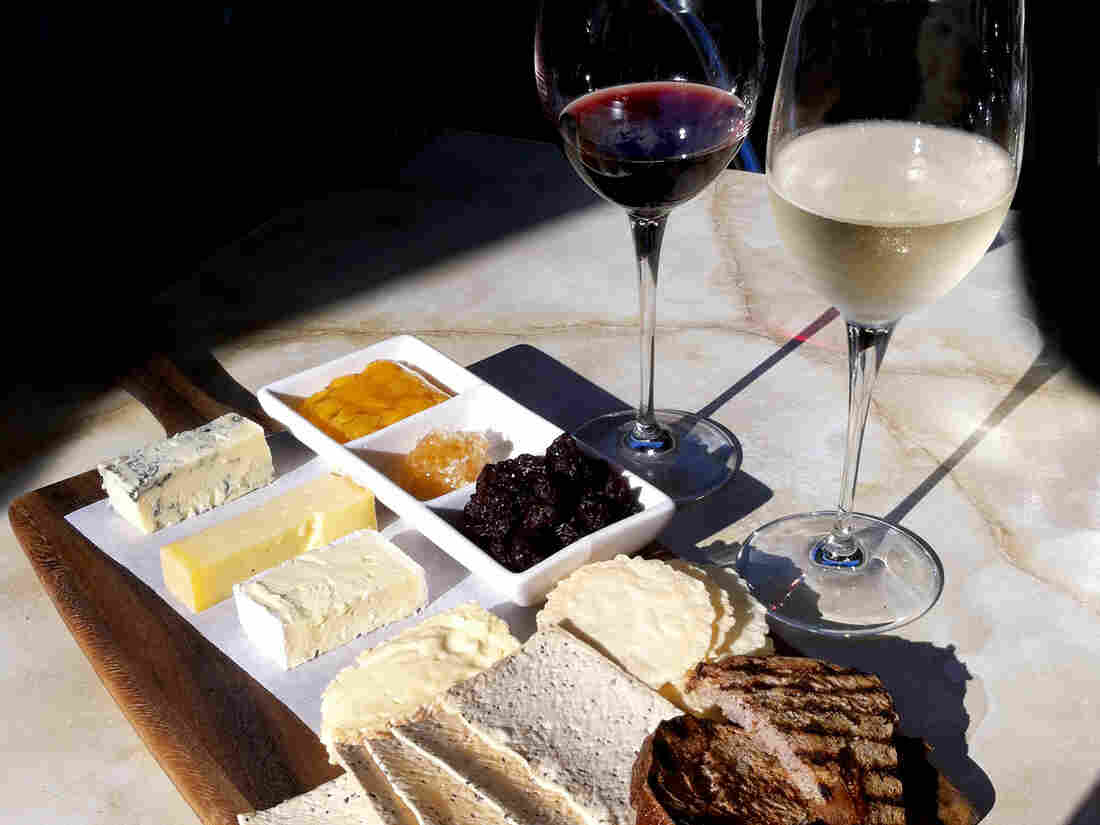 Red and white wine in glasses with a cheese platter of a variety of cheeses with crackers and bread