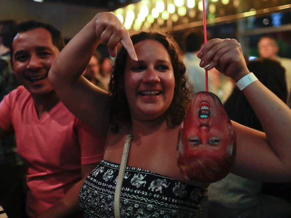 A woman at a bar in Buenos Aires, Argentina, laughs as she holds a mask depicting Donald Trump during an election night party on Nov. 8. (Natacha Pisarenko/AP)